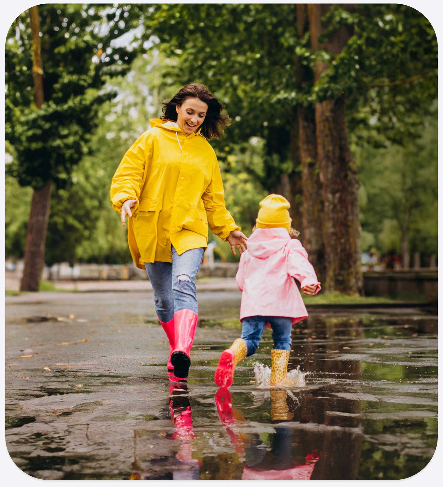 Mamma e bambina che giocano all’aperto sotto la pioggia indossando impermeabili colorati