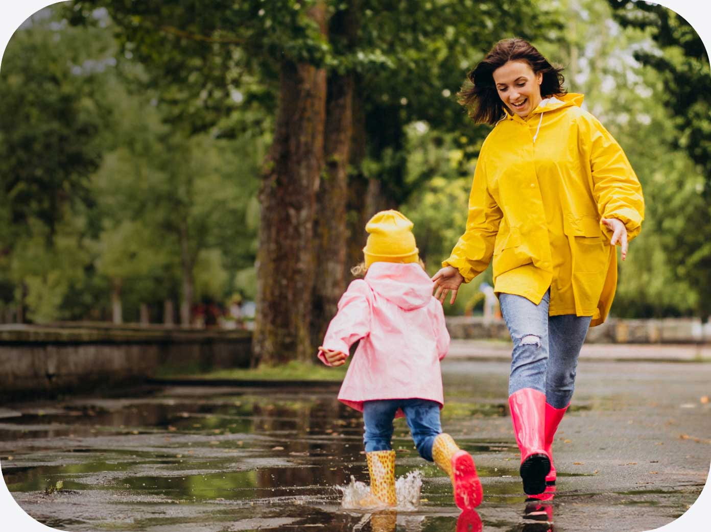 Mamma e bambina che giocano all’aperto sotto la pioggia indossando impermeabili colorati