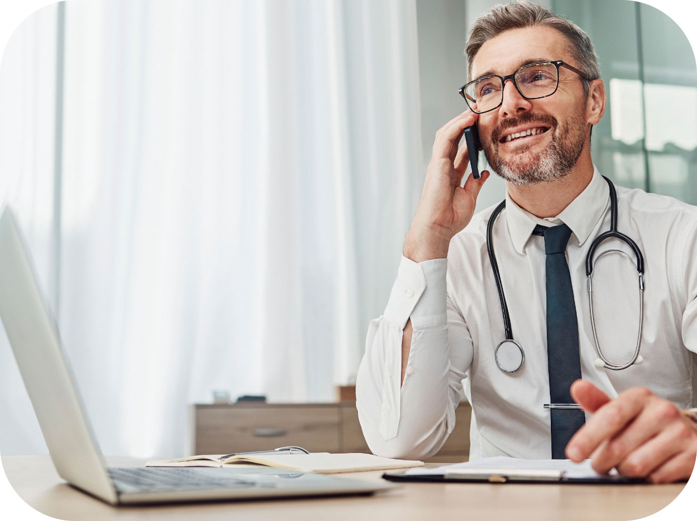 Medico che parla al telefono durante una consulenza mentre è seduto davanti al computer